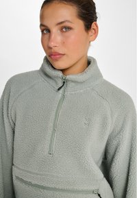 Fleece pullover in lichtgroen met een halfrits ontwerp, gestructureerd materiaal en een ritssluiting aan de voorkant. Voorzien van een klein logo.