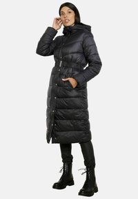 Černý péřový kabát s kapucí, opaskem v pase, zapínáním na patentky a bočními kapsami. Má prošívanou texturu a dlouhé rukávy.