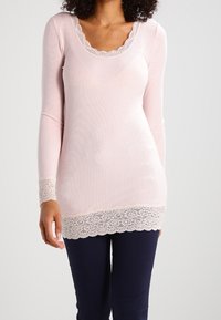 Vaalea vaaleanpunainen pitkähihainen paita, jossa on avara kaula-aukko ja pitsireunus helman ja hihojen reunassa, valmistettu ribbieristymästä, sovitettu malli.