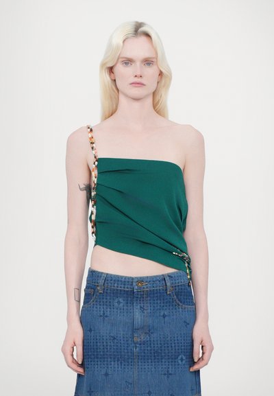 Top verde sin mangas con tejido drapeado y detalle de tirante decorado con cuentas, combinado con una falda de mezclilla con un patrón texturizado.
