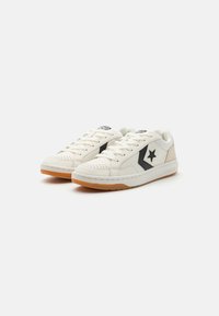 White leather sneakers with black and beige accents. Features a star logo, perforated toe, and gum rubber sole. Lace-up design.