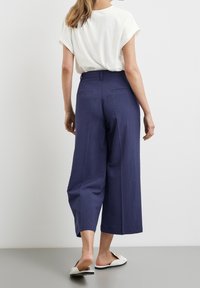 Brede marineblauwe broek van lichtgewicht stof, met een hoge taille, zijzakken en achterzakken met paspel, gecombineerd met een wit top.