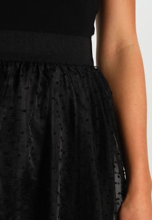 Zwarte rok met een gestructureerde, doorschijnende laag met polkadots. Elastische tailleband zorgt voor een stevige pasvorm. Zachte, lichtgewicht stof.