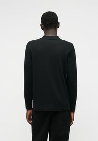 Μαύρος μακρυμάνικος πουλόβερ με κλασικό γιακά, κατασκευασμένο από απαλό πλεκτό υλικό. Παρουσιάζει ευθείες γραμμές και ριπές στους καρπούς και το στρίφωμα.