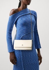Abito blu a coste con design off-shoulder; borsa a tracolla in pelle bianca con logo dorato e tracolla metallica.