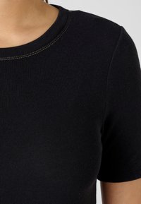 Black short-sleeve T-shirt with a ribbed texture and a round neckline, featuring contrasting yellow stitching along the collar.