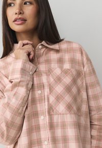 Roze geruit overhemd van zachte stof, met een knoopsluiting aan de voorkant, lange mouwen en een opgestikte zak aan de linkerkant.