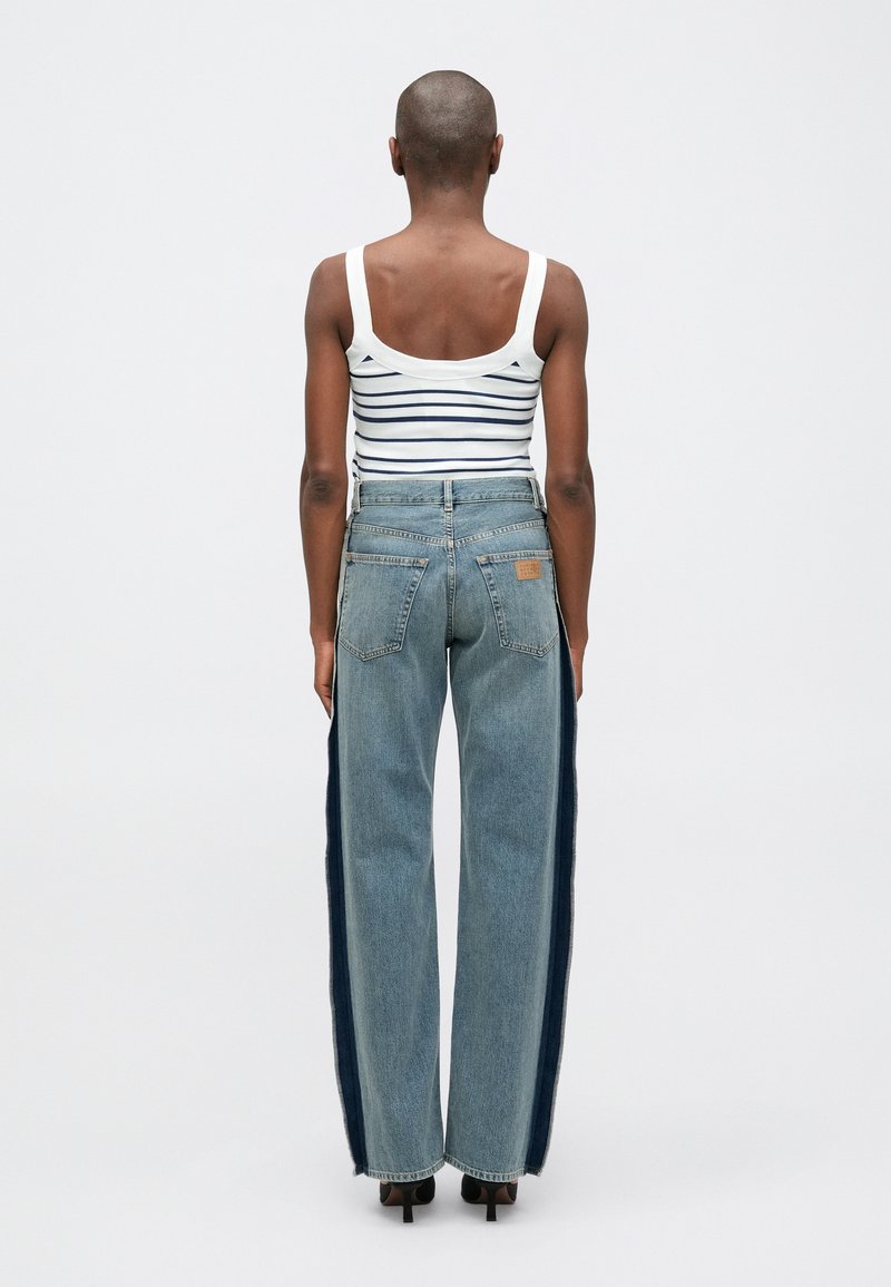 Randig, ärmlös vit topp i kombination med högmidjade blå denimjeans med mörkare sidostripes och en rak passform.