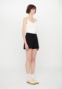Pantalones cortos negros con cintura ajustable, combinados con una camiseta sin mangas blanca y zapatillas beige. Tejido suave, diseño casual.
