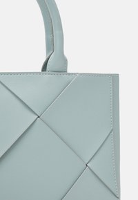 Lyseblå læderhandske med et geometrisk quiltet design, der har robuste håndtag og kontraststikninger for ekstra detaljer.