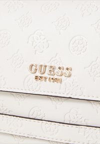 Borsa Guess bianca in rilievo con logo dorato, superficie testurizzata con motivi intricati e cuciture nere lungo i bordi.
