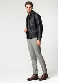 Czarna skórzana kurtka z kołnierzem stojącym, noszona na ciemnej bluzce. Szare w kratkę spodnie oraz brązowe sznurowane botki dopełniają ubranie.