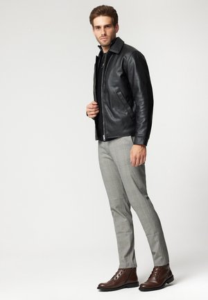 Czarna skórzana kurtka z kołnierzem stojącym, noszona na ciemnej bluzce. Szare w kratkę spodnie oraz brązowe sznurowane botki dopełniają ubranie.