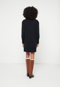 Vestido de malha azul-marinho com mangas compridas e bainha canelada, combinado com botas de couro castanhas até ao joelho, com acabamento branco e saltos quadrados.