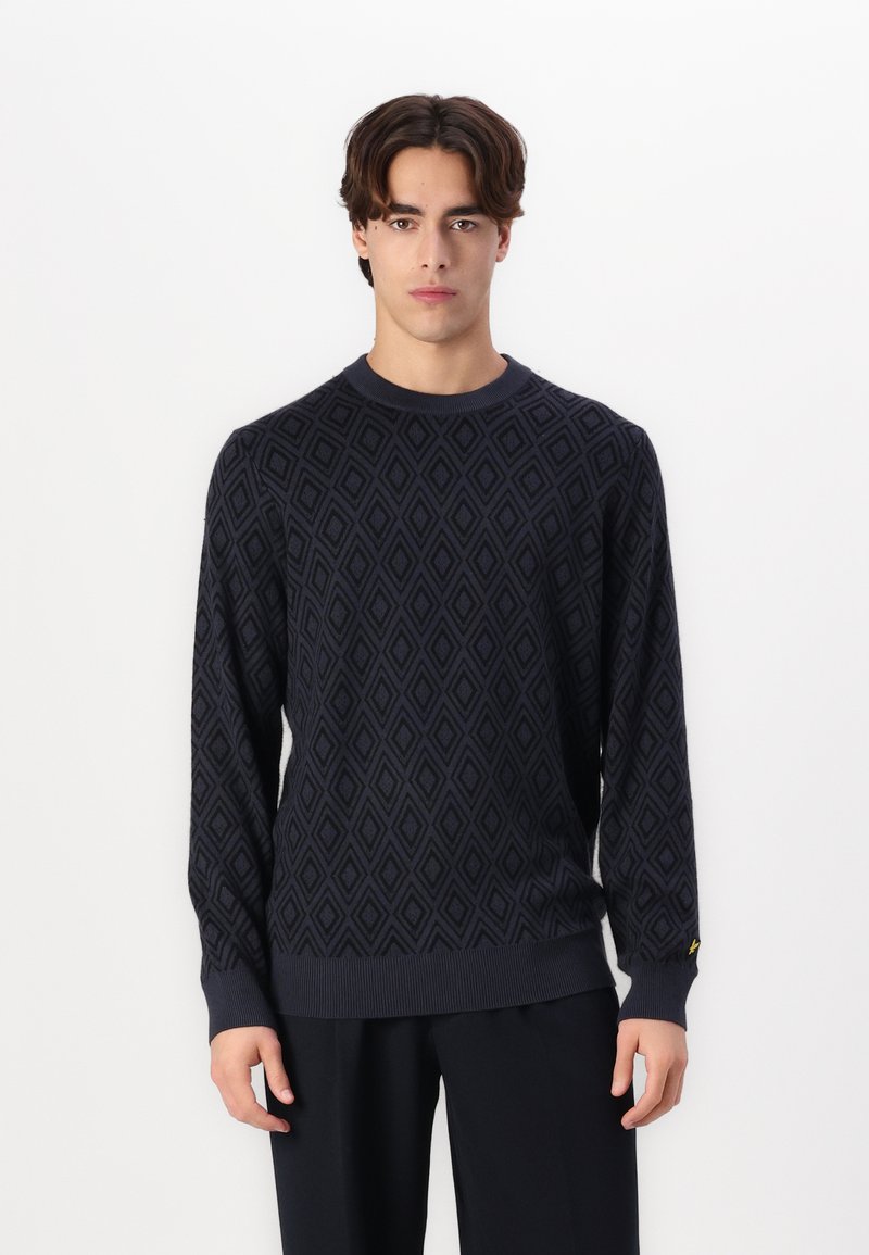 Navyblauwe gebreide trui met een ruitpatroon, geribde boorden en zoom, en een klein accentdetail op de mouw.