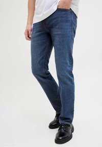 Jeans de mezclilla azul con un corte ajustado, diseño de cinco bolsillos, costuras en contraste y combinados con zapatos negros de cordones.