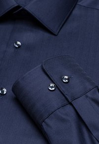 Marineblauw herringbone patroon shirt met een gestructureerde kraag, voorzien van metalen knopen en een omgeslagen manchet. Soepele stoftextuur.