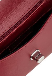 Burgundska usnjena torbica z teksturiranim zaključkom, ki ima žep na zadrgo in srebrne kovinske detajle. Notranjost je iz črnega blaga.