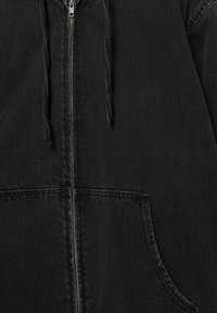 Veste en denim noire avec fermeture éclair avant, capuche avec cordon de serrage et poche kangourou visible en gros plan.