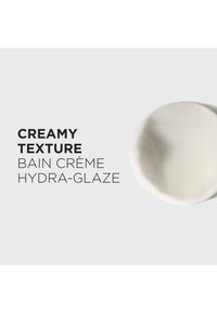 Witte romige cosmetische productveeg naast vetgedrukte tekst "Romige Textuur Bain Crème Hydra-Glaze" op een lichtgrijze achtergrond.