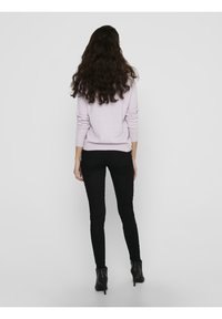Pull violet clair à manches longues, ourlet côtelé. Associé à un jean skinny noir et des bottines noires, vu de dos.