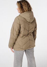 Bruine gewatteerde pufferjack met een capuchon, voorzien van een geometrisch patroon en elastische manchetten. De achtergrond is eenvoudig wit.