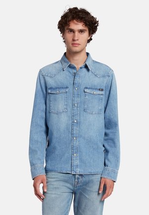 Light blue denim shirt with long sleeves, chest pockets, pointed collar, and front silver buttons. Smooth texture and classic design.
