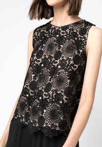 Svart spetsblus med blommönster, vågig nederdel och ärmlös design. Bakgrunden är ljus.