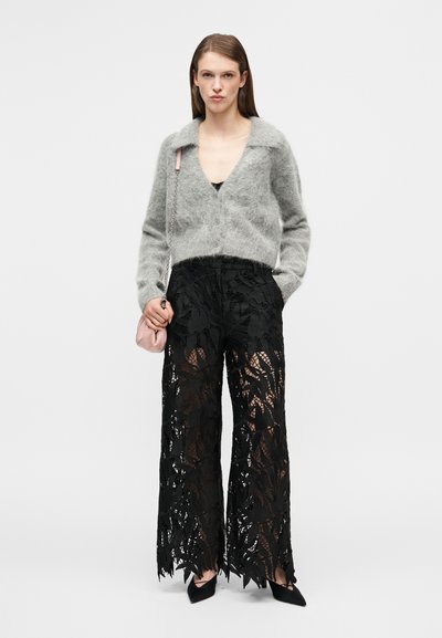 Γκρι πλεκτή ζακέτα με φαρδύ γιακά, συνδυασμένη με ψηλόμεσο μαύρο δαντελένιο παντελόνι με λουλουδένιο σχέδιο. Συμπληρώνεται με μια μικρή ροζ τσάντα.
