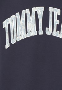 Navy sweatshirt featuring white and light blue floral patterned "TOMMY JEANS" text. Soft fabric with a smooth texture.