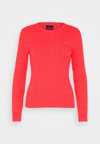 Bright coral red cable-knit crewneck sweater with long sleeves and ribbed cuffs and hem, featuring a small embroidered logo on the chest.