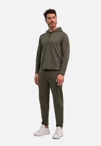 Felpa verde oliva con cappuccio e maniche lunghe, abbinata a pantaloni jogger tapered coordinati. Sneakers bianche completano l'outfit casual.