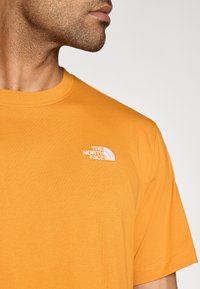 Κοντομάνικο, μπλουζάκι με στρογγυλή λαιμόκοψη από φωτεινό πορτοκαλί βαμβάκι. Διαθέτει μικρό λευκό λογότυπο στο αριστερό μέρος του στήθους. Ομαλή υφή, μινιμαλιστικός σχεδιασμός.