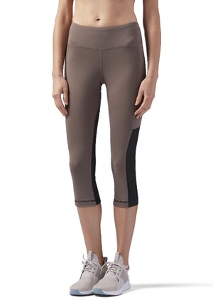 Leggings capri marron avec taille haute, dotés de panneaux latéraux en maille noire et de coutures plates, associés à des chaussures de sport claires.