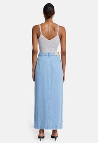Lichtblauwe denim maxi-rok met een hoge taille en een rechte snit, gecombineerd met een strak grijs geribd tanktop. Kleine details op de tailleband.