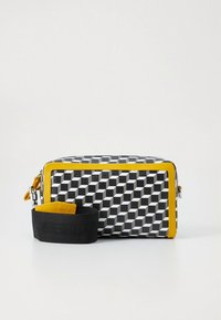 Sac à motifs géométriques noir et blanc avec accents jaunes, forme rectangulaire, matériau texturé et bandoulière noire amovible.