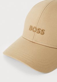 Casquette de baseball beige avec un design structuré, arborant un logo "BOSS" brodé dans une teinte assortie et des détails de coutures visibles.
