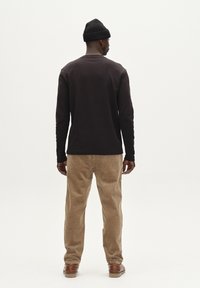 Donkere trui met lange mouwen en een ronde hals, gecombineerd met lichtbruine corduroy broek met textuur. Het model draagt een zwarte gebreide beanie.