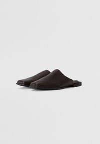 Dark brown slip-on mules with a textured, reptile-like pattern, rounded toe, and flat sole featuring a small lip at the back.
