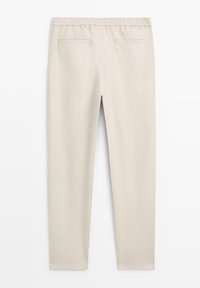 Lichtbeige elastische broek met rechte pijpen en twee achterzakken met paspels, gezien van achteren.