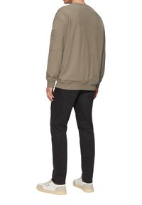 Olijfgroene sweatshirt met een ronde hals, geribbelde manchetten en een patchzak op de mouw, gecombineerd met zwarte jeans en witte sneakers.