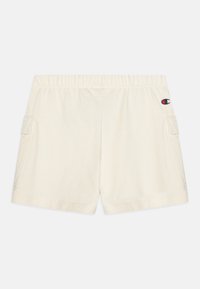 Bermudas de algodón color crema con cintura elástica, bolsillos laterales y un pequeño parche de logo en la parte trasera derecha. Textura suave.