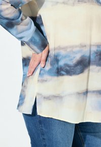 Lichtgewicht lange mouw shirt in crème met blauw tie-dye patroon, met een zijsplit aan de onderkant en knoopdetails op de manchetten.