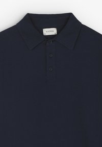 Polo azul marino hecho de algodón, con un cuello clásico, una tapeta de tres botones y una textura suave. La etiqueta dice "SCALPERS."