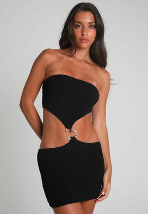 Schwarzes Strickkleid mit einem trägerlosen Design, Ausschnitten in der Taille und metallischen Ringakzenten in der Mitte und am unteren Saum.
