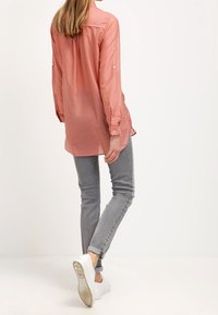 Ljust rosa långärmad skjorta med knappat krage, bakveck och rullade ärmar, kombinerad med grå slim-fit jeans och vita sneakers.