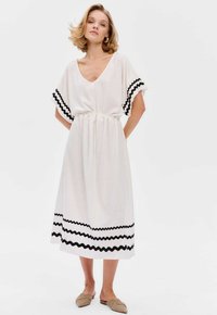Witte knie-lange jurk met een V-hals, korte mouwen met zwarte zigzagaccenten, een getailleerde taille en een vloeiende silhouet.