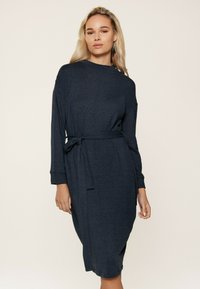 Abito lavorato a maglia blu navy con maniche lunghe, scollatura rotonda e una cintura in tessuto coordinato annodata in vita, caratterizzato da una vestibilità rilassata e tasche laterali.