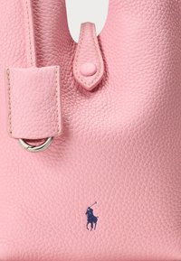 Rožinė tekstūruota odinė rankinė su apvalia sidabrine detalė ir tamsiai mėlynu polo žaidėjo logotipu. Įrengta užsegama sklende ir siuvinėtais akcentais.