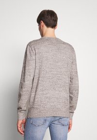 Grauer Strickpullover mit Rundhalsausschnitt, langen Ärmeln und strukturierter Oberfläche. Wird mit blauen Jeans getragen und zeigt einen lässigen Schnitt von hinten.